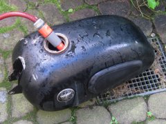 Der entrostete Motorradtank wird mit Wasser aus dem Gartenschlauch gespült.