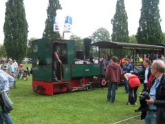 Ein Feldbahn–Dampfzug am Rebstockgelände, im Hintergrund Straßen–Oldtimer.