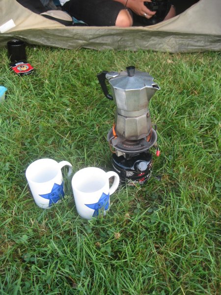 Kaffeemaschine auf einem Benzinkocher und zwei Tassen im Gras.