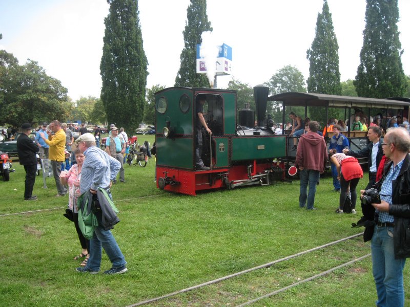 Ein Feldbahn–Dampfzug am Rebstockgelände, im Hintergrund Straßen–Oldtimer.
